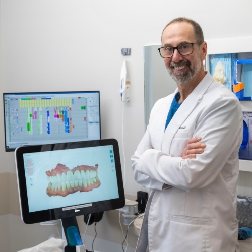 Smiling dentist standing next to monitor showing digital model of teeth