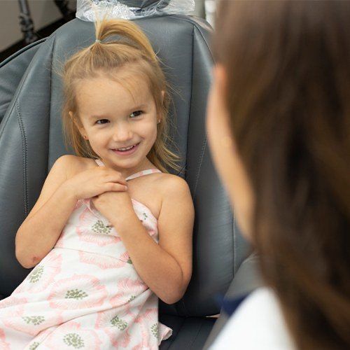 Young girl in dental chair grinning at her dentist