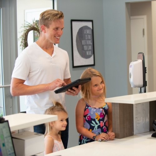 Father and two daughters checking in at dental office front desk