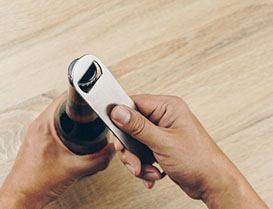 Person using a bottle opener on a glass bottle