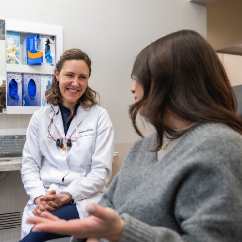 Dentist smiling at woman in dental chair with gray sweater