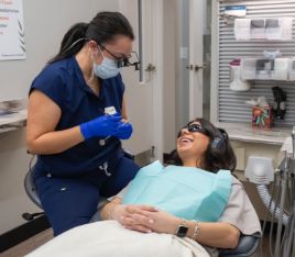 Woman in dental chair with sunglasses and blanket talking to dental team member