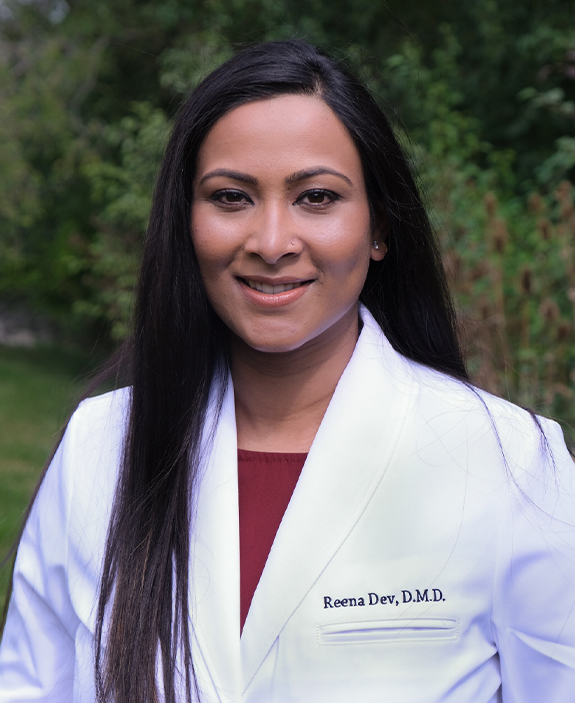 Doctor Reena Dev smiling in white lab coat outdoors