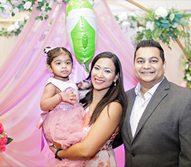 Doctor Dev smiling at formal event with her husband and baby daughter